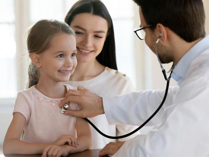 A doctor uses a stethoscope to check a smiling child's heart.