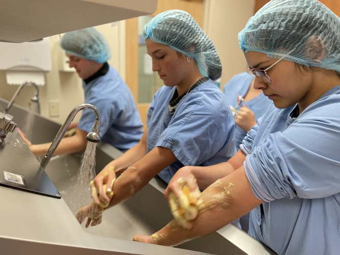 Three women in scrub suits washing hands with soap sink in Le Mars, IA
